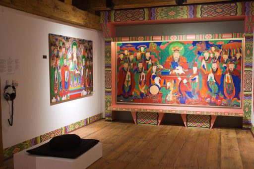 Wystawa "Sztuka Dalekiego Wschodu" w Pichlerzu. Jedna z muzealnych sal. Drewniana podłoga, białe ściany, na nich dużych rozmiarów kolorowe malowidła koreańskie przedstawiające postacie pochodzące z wierzeń tego regionu.