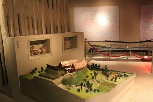 Sala wystawy "X wieków Płocka" muzeum, makieta słowiańskiej wioski - zielone wzgórza, mały staw i drewniane zabudowania z dachami ze słomy.