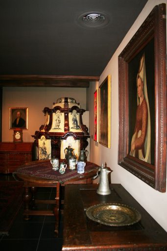 Sala wystawy "X wieków Płocka" muzeum. Wnętrze z dużym barokowym piecem z ozdobnymi kaflami z niebieskimi malunkami oraz sarmackimi portretami na ścianie.