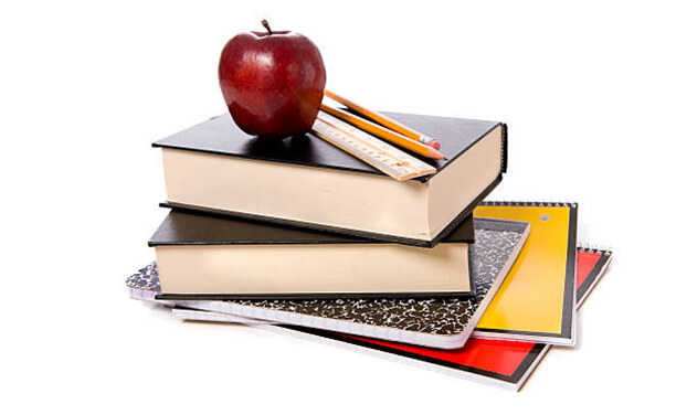 Zdjęcie poglądowe - stos książek i zeszytów, na nim linijka, ołówki i czerwone jabłko.