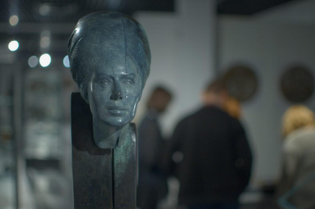 Zdjęcie z wernisażu wystawy rzeźb i medali, na pierwszym planie zbliżenie na rzeźbę przedstawiającą głowę kobiety w dużym turbanie.