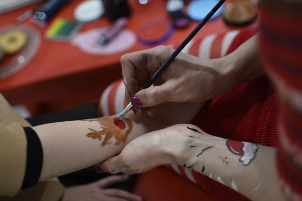 Zbliżenie na dłonie praz przedramiona dorosłej kobiety i dziecka. Dłonie kobiety malują na przedramieniu dzieciak świąteczną dekorację. 