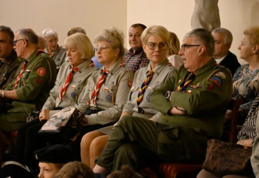 Patio Muzeum Mazowieckiego w Płocku, na ustawionych w rzędy krzesłach siedzą dorosłe osoby w harcerskich mundurach.