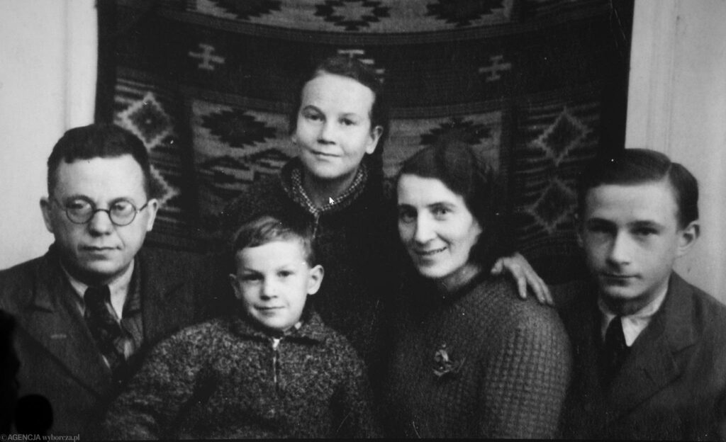 Archiwalne zdjęcie rodzinne Ładysława Żelazowskiego, on sam siedzi po lewej stronie, ma ciemne włosy, garnitur i okulary. Obok niego wie kobiety, młody mężczyzna i dziecko. Wszyscy uśmiechają się do obiektywu.