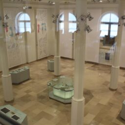 Sala Muzeum Żydów Mazowieckich, jasne ściany i podłoga, wysokie okna, kolumny i multimedialne kioski.