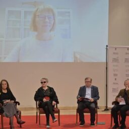 Aula muzeum, scena, na niej cztery krzesła. Siedzą na nich od lewej - Małgorzata Sady, Maya Gordon, Leonard Sobieraj, Andrzej Pościański. Za nimi na ścianie ekran, na nim widoczna Ingrid Blakestad.